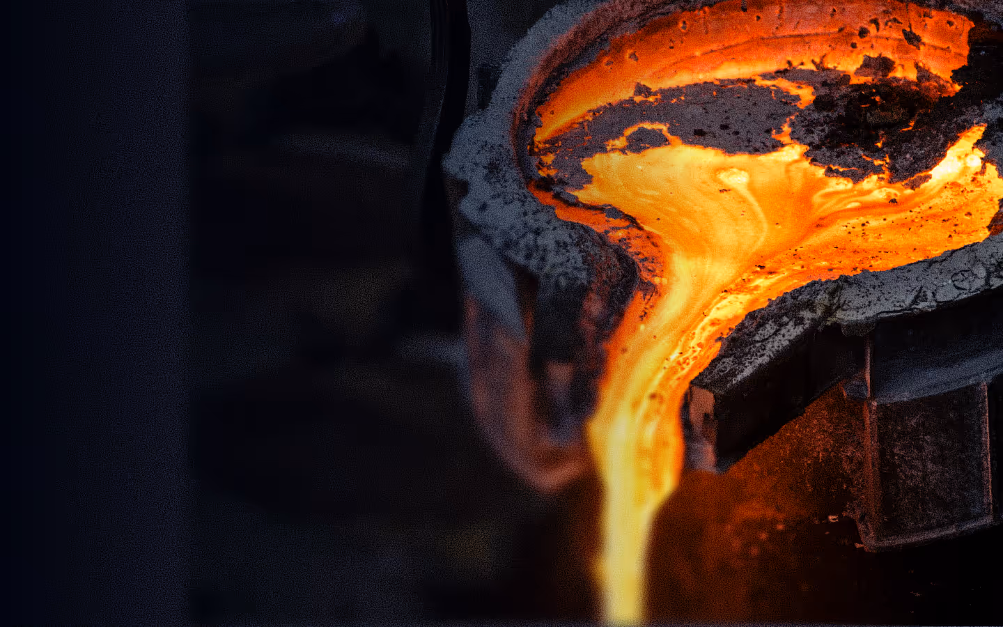 Molten metal being poured from a heated crucible in a dark industrial setting.