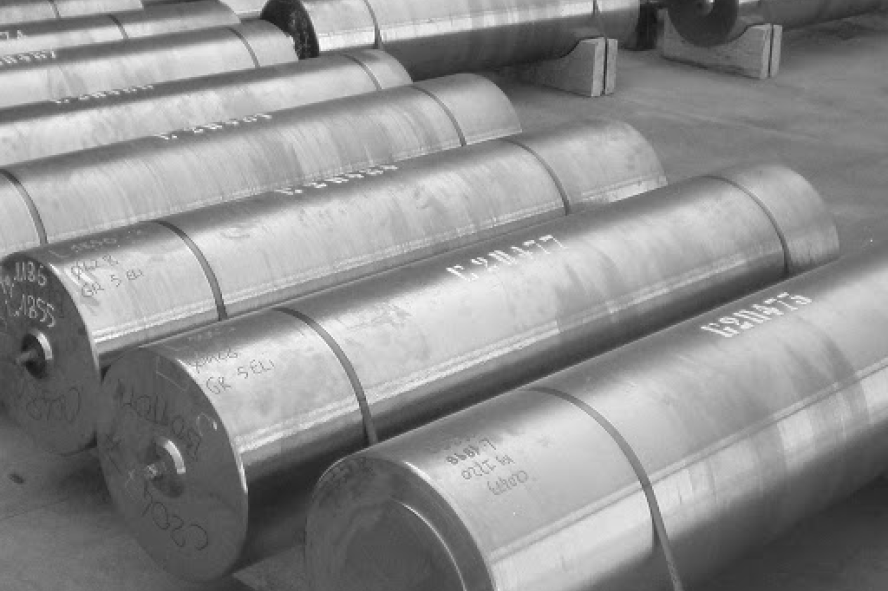 Rows of large cylindrical metal rods with markings, stacked on a factory floor.