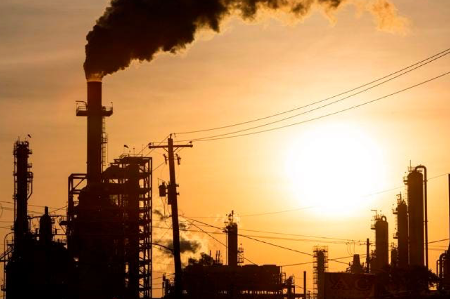 Industrial factory with smokestacks emitting dark smoke against a sunset sky.